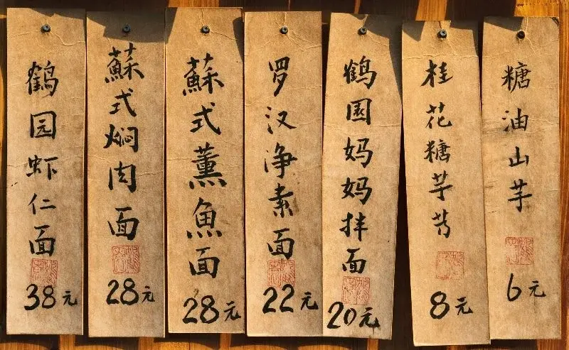 Hand-lettered wooden price tags at a Suzhou noodle shop listing dishes and prices in yuan
