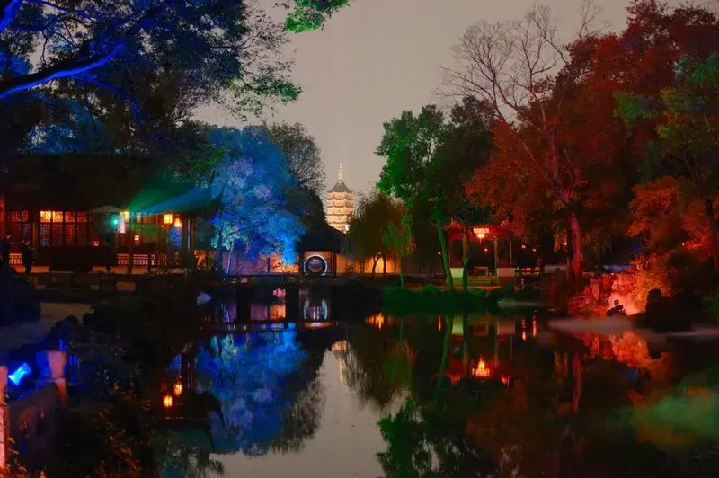 A classical Suzhou garden pavilion with pond, rockery and pine trees, seen from a covered walkway