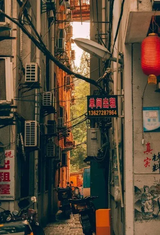 A narrow Wuhan alley lined with air-conditioning units and a red sign advertising a single room for rent, a red lantern hanging nearby