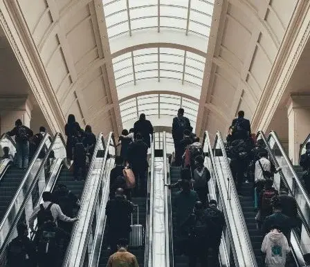 A dense crowd of commuters and travelers with luggage riding a bank of escalators inside a Wuhan train station