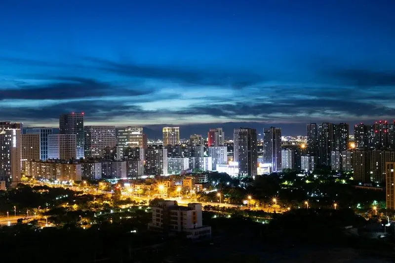 A dense skyline of Xiamen apartment towers lit up at night against a dark blue sky