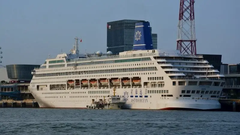 A large white cruise ship docked at Xiamen's international port terminal, with the modern skyline behind it