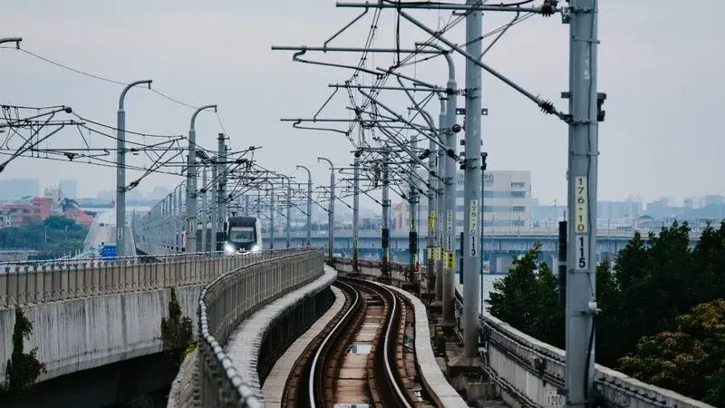 An elevated Xiamen Metro train on a curved viaduct with the sea and coastline visible in the background
