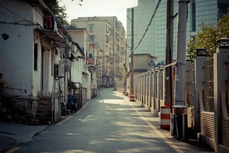 A quiet street with older low-rise buildings on one side and a construction fence with a new high-rise behind it on the other