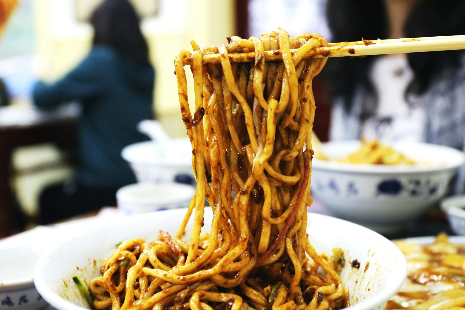 Chopsticks lifting a tangle of sauce-coated hand-pulled noodles from a bowl