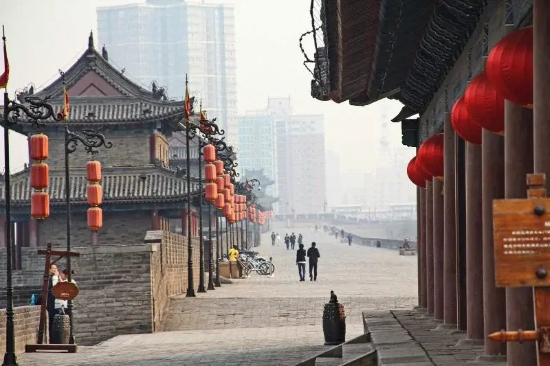 The walkway atop Xi'an's Ming city wall, lined with red lanterns, modern high-rises in the haze beyond