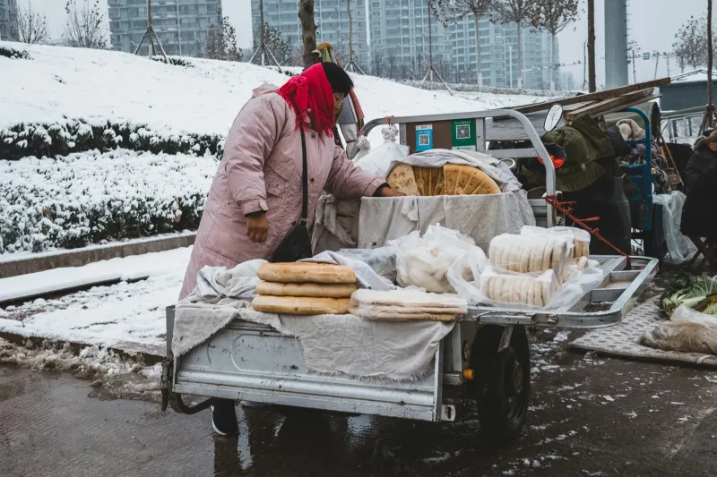 A street vendor stacking flatbread on a cart at a snowy winter morning market in a northern Chinese city