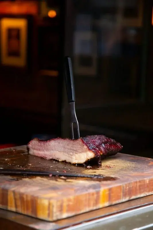 A slab of smoked Texas brisket resting on a wooden board with a carving fork