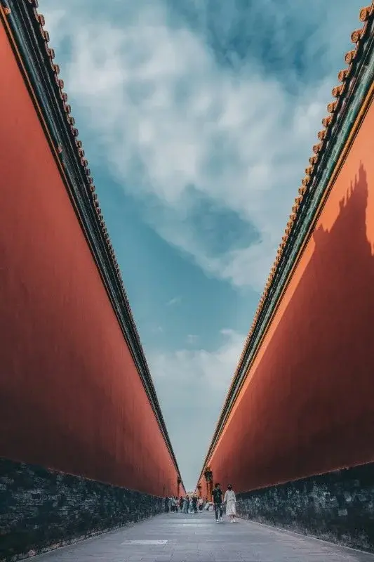 A long corridor between two vermilion Forbidden City walls, visitors walking toward the vanishing point