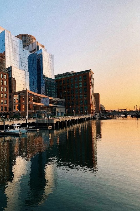 Boston's Seaport waterfront along Fort Point Channel at sunset, glass towers reflected in the water