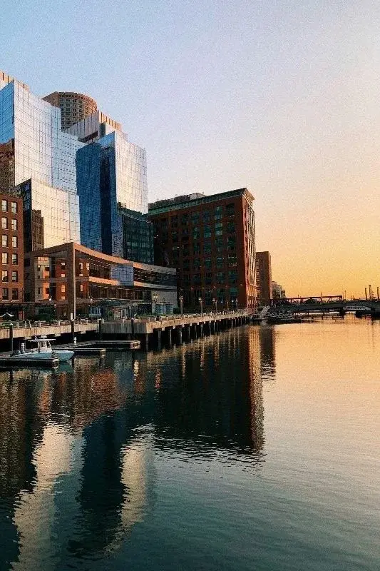 Boston's Seaport waterfront along Fort Point Channel at sunset, glass towers reflected in the water