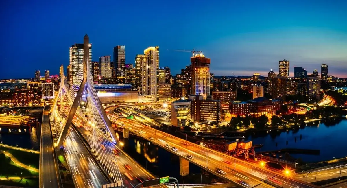 Boston skyline at night from the Zakim Bridge, with light trails on the highway below