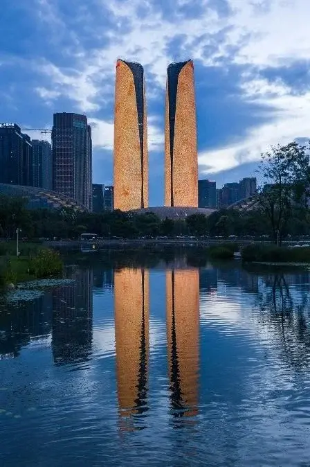 Two curved, illuminated tower buildings reflected in a lake in Chengdu at dusk
