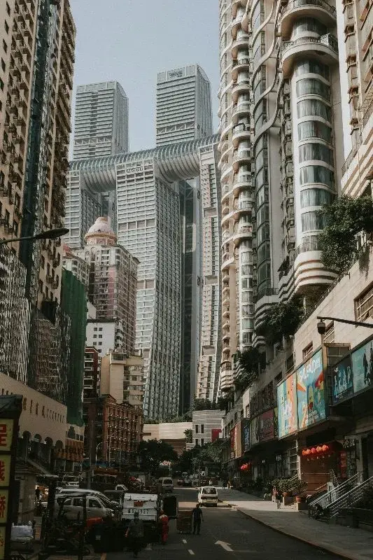 A canyon of Chongqing high-rise towers seen from street level, including a curved connecting structure joining two towers, with red lanterns visible on a shopfront below