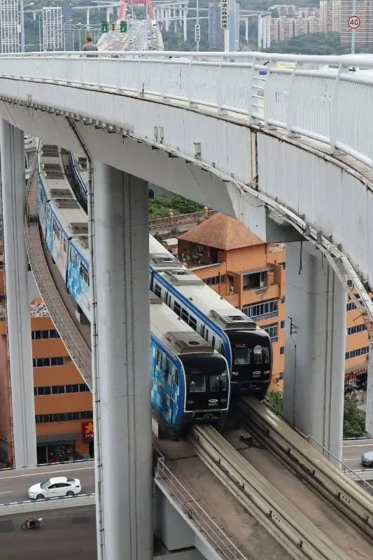 A Chongqing monorail train on an elevated curved viaduct threading between buildings, with a road bridge running above it
