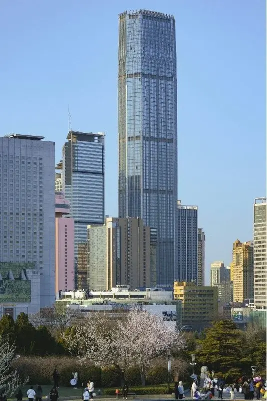 A Dalian office and apartment tower, one of the city's tallest buildings, seen against a clear blue sky with cherry blossoms below