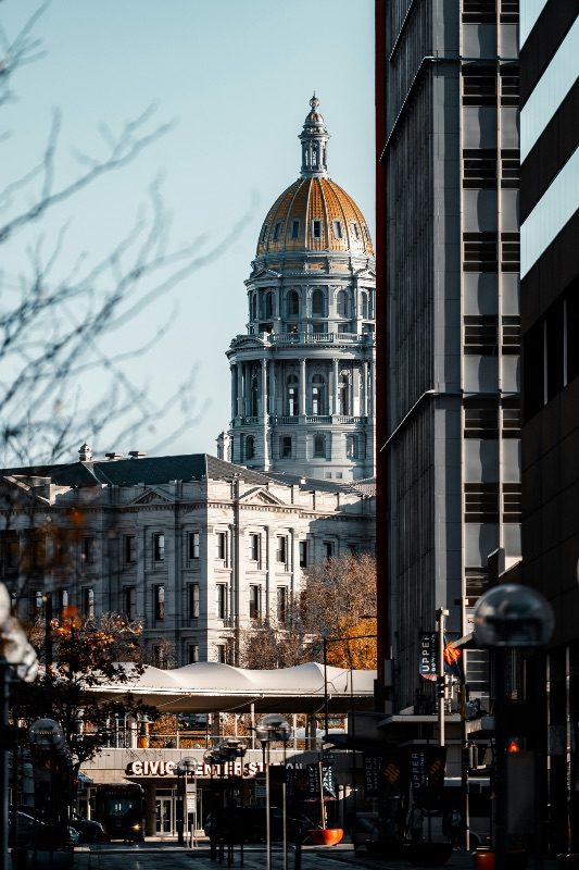 The gold dome of the Colorado State Capitol seen between downtown Denver office towers