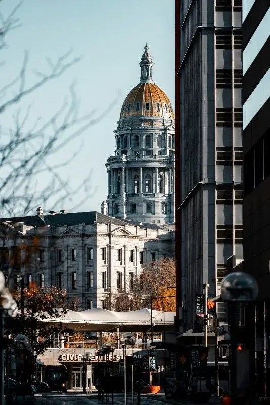 The gold dome of the Colorado State Capitol seen between downtown Denver office towers