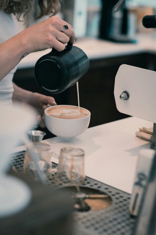 A barista pouring latte art into a cup at a Denver coffee bar