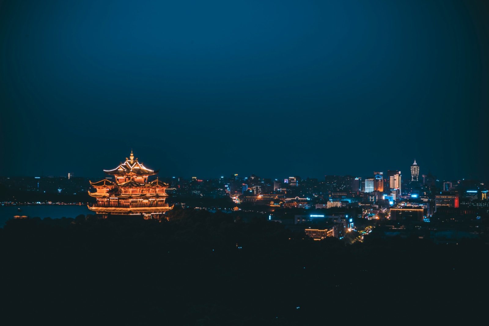 West Lake in Hangzhou at night with a lit pagoda and the city skyline behind it