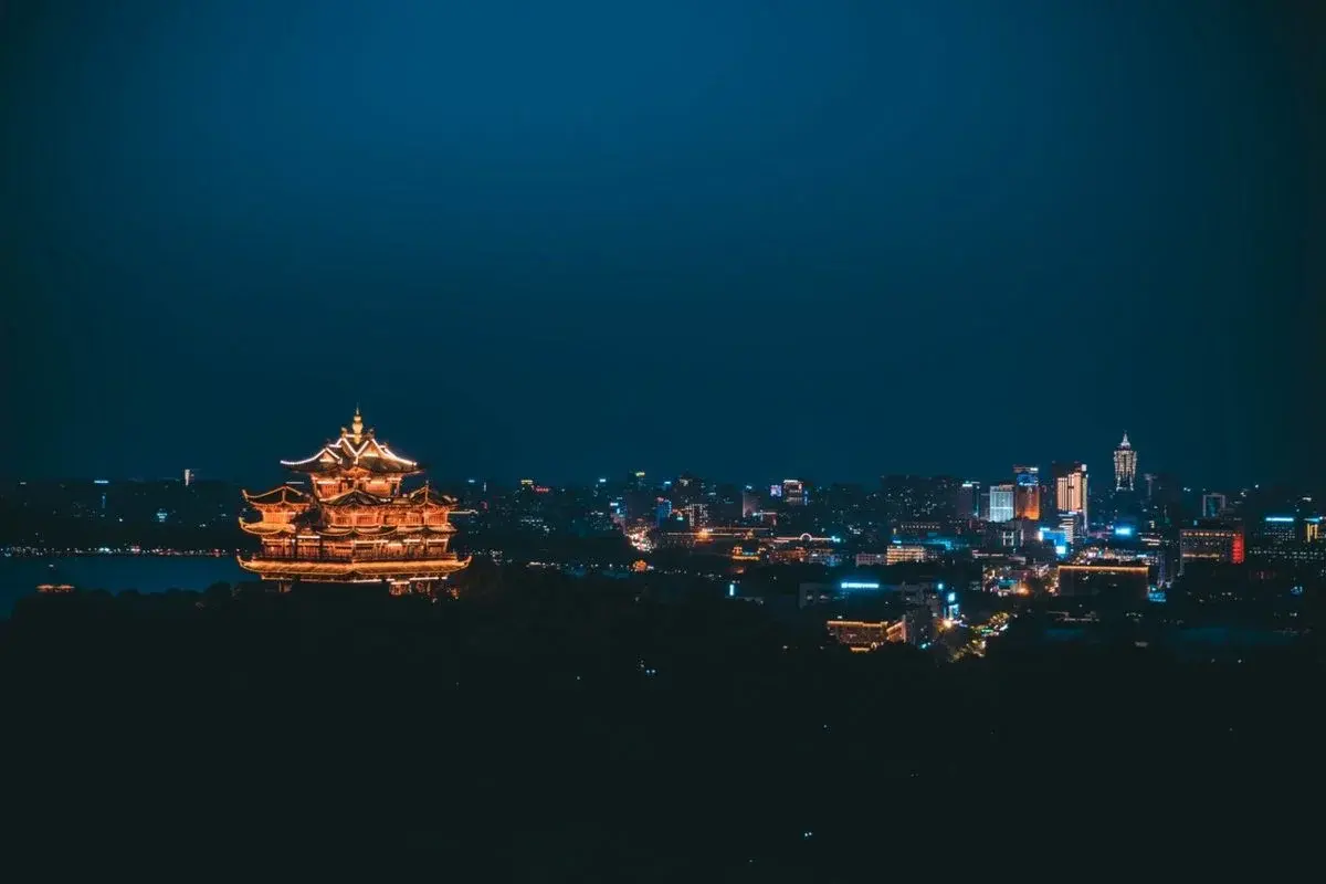 West Lake in Hangzhou at night with a lit pagoda and the city skyline behind it