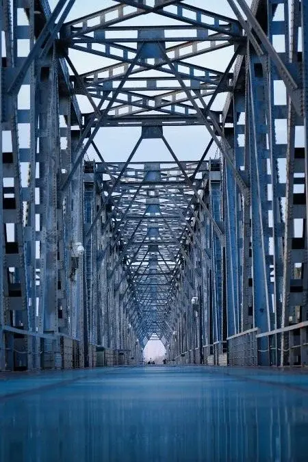 A steel truss bridge over a river in Harbin, converging lines of girders leading toward the far bank