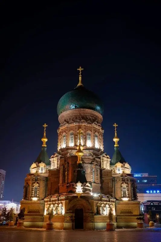 Saint Sophia Cathedral in Harbin lit up at night, its green onion dome and crosses illuminated against a dark sky