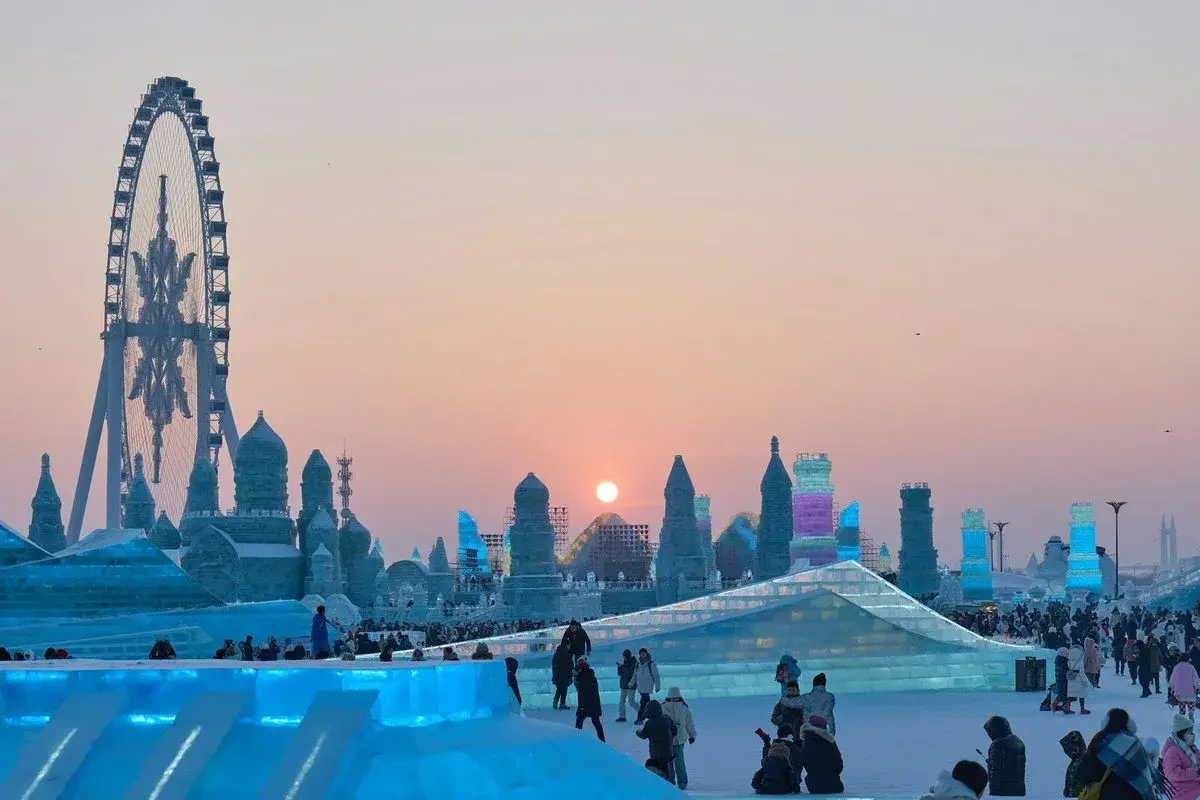 Harbin's Ice and Snow World at sunset, ice towers lit blue and purple, crowds on the ice