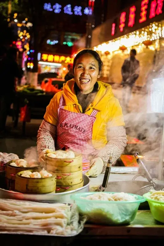 A street food vendor steaming buns and noodles at a night market stall in Kunming