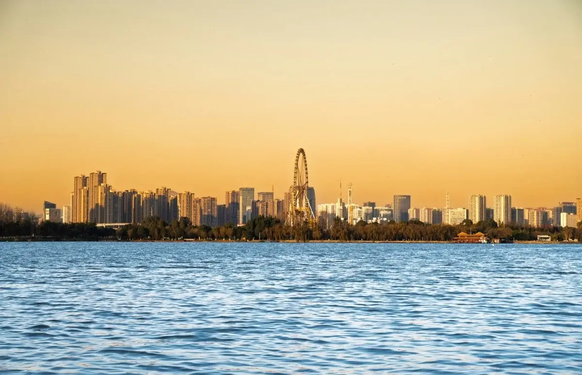 Kunming's skyline at sunset seen across Dianchi Lake, with a Ferris wheel silhouetted among the towers