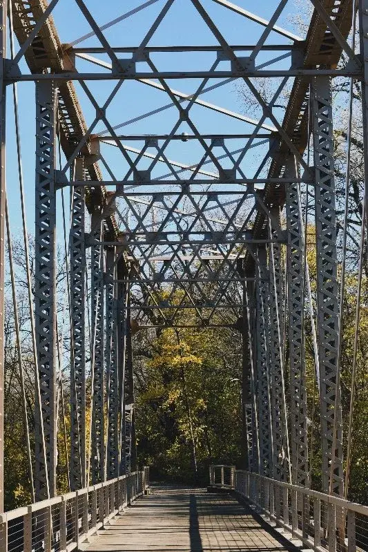 A steel truss pedestrian bridge in Minneapolis, autumn trees visible through the far end