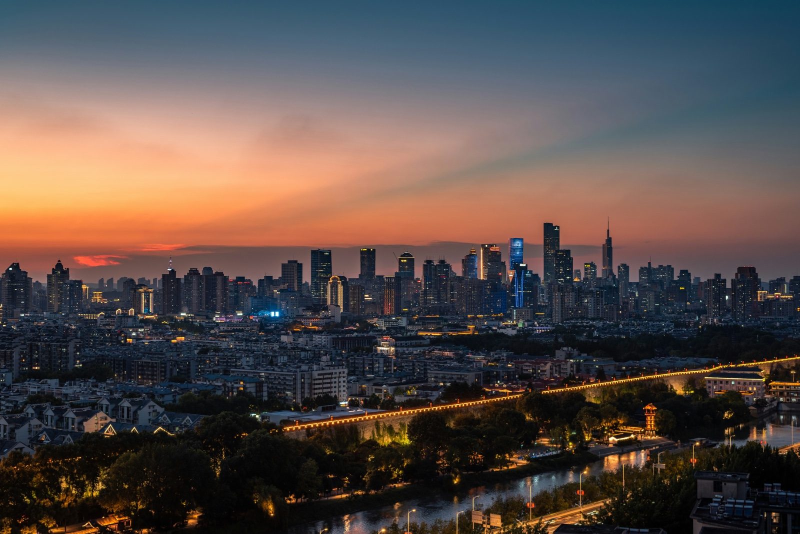 Nanjing's skyline at dusk, the illuminated Ming city wall and moat running along the foreground with the modern downtown towers lit up behind