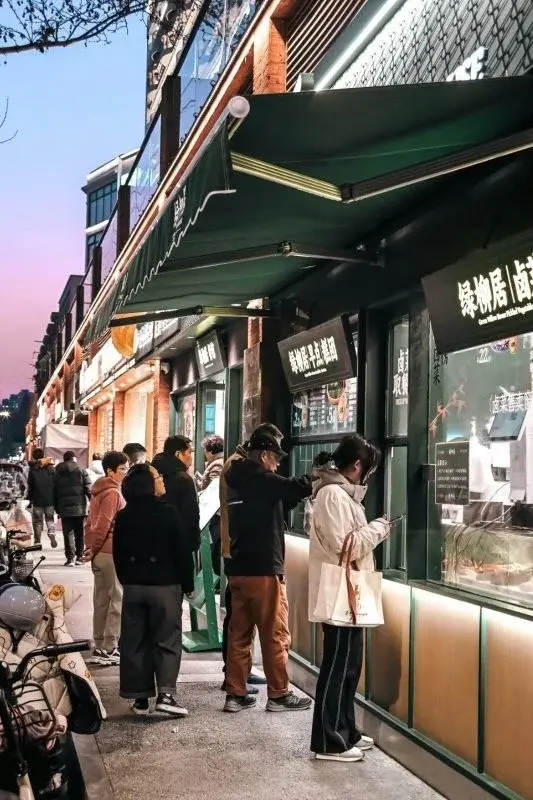 A Nanjing street food counter at dusk, customers lined up ordering pickled vegetables and prepared dishes through a service window