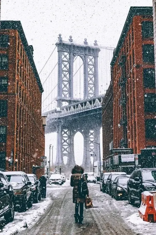 A snow-covered DUMBO street in Brooklyn with the Manhattan Bridge framed between two brick warehouse buildings