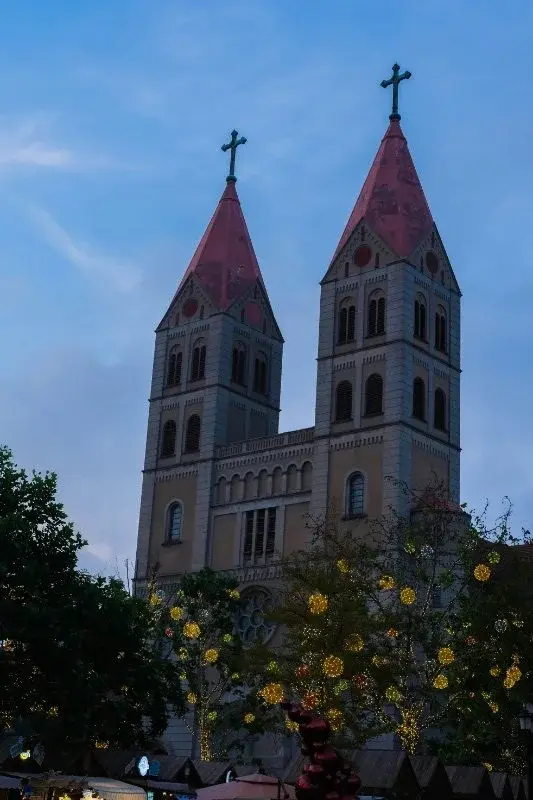 The twin red-roofed spires of St. Michael's Cathedral in Qingdao, lit at dusk with holiday lights in the trees below
