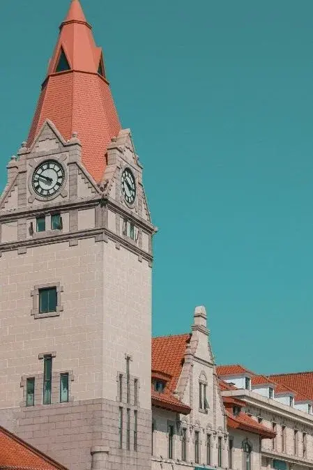 The clock tower of Qingdao's German-built railway station, red tile roof against a clear sky