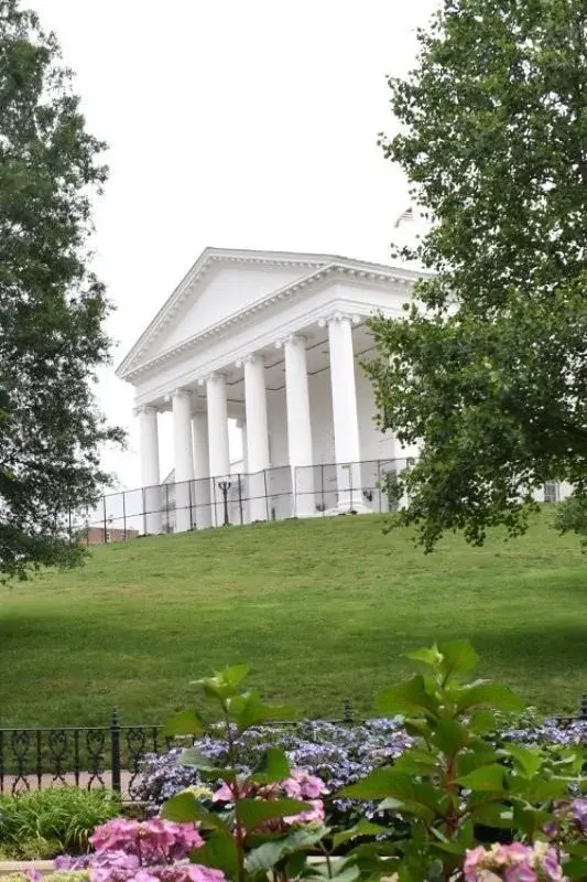 The Virginia State Capitol's Neoclassical columned portico, seen across a lawn and gardens in Richmond