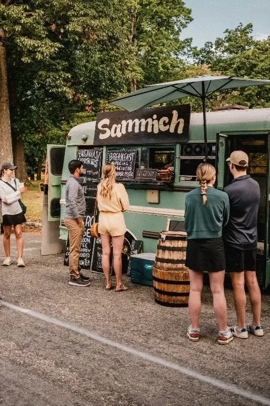 Customers ordering at a green vintage food truck called Sammich, parked under trees at a Richmond outdoor market