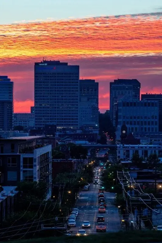 A Richmond street at dusk, downtown office towers silhouetted under a burning orange sunset sky