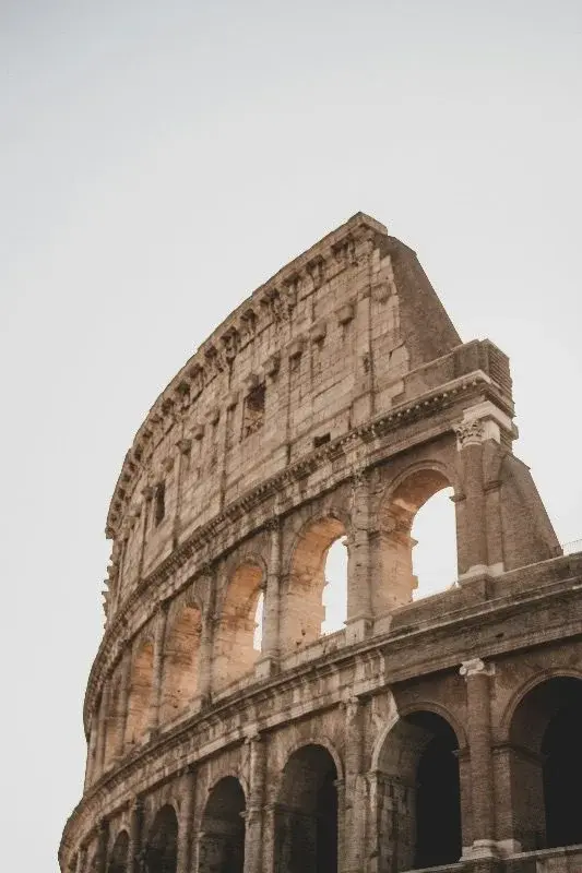 Close-up of the Colosseum's upper arches and travertine facade against a pale sky