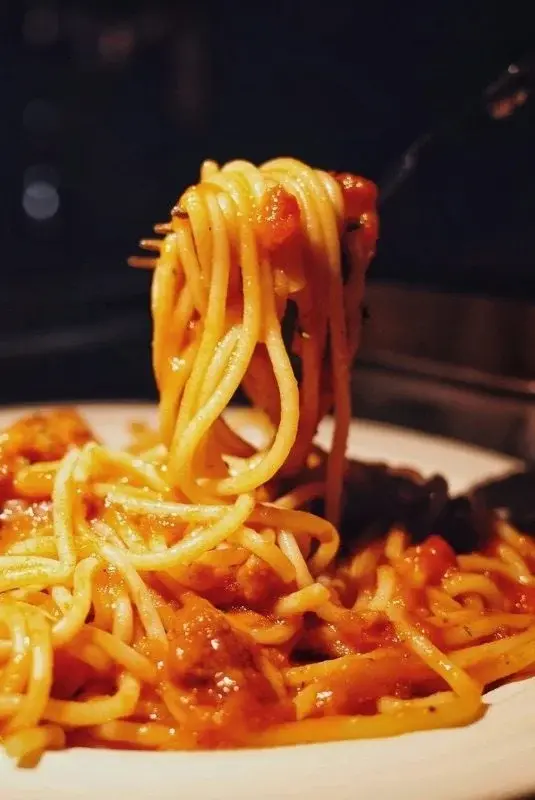 A fork lifting tomato-and-meat-sauce spaghetti from a plate, dark restaurant setting behind