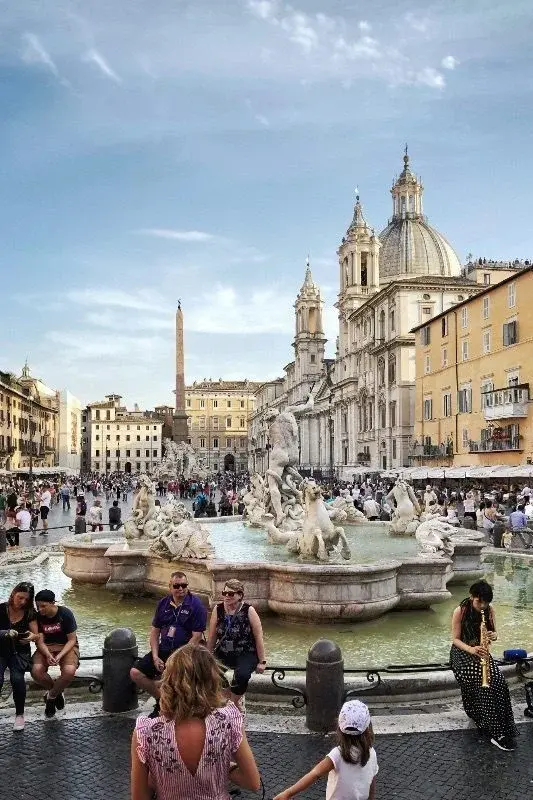 Piazza Navona in Rome, with the Fountain of the Four Rivers, an obelisk, and Sant'Agnese in Agone's dome behind evening crowds