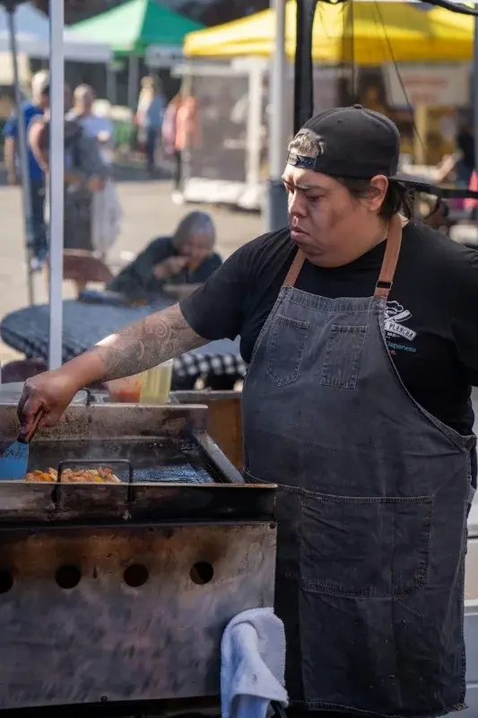 A cook working a griddle at an outdoor street food stand in San Diego