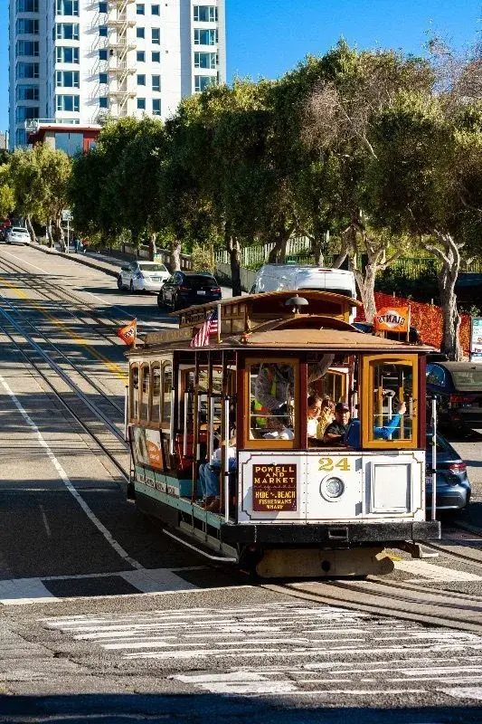A San Francisco cable car, the Powell and Market Line 24, climbing a hill street with passengers aboard