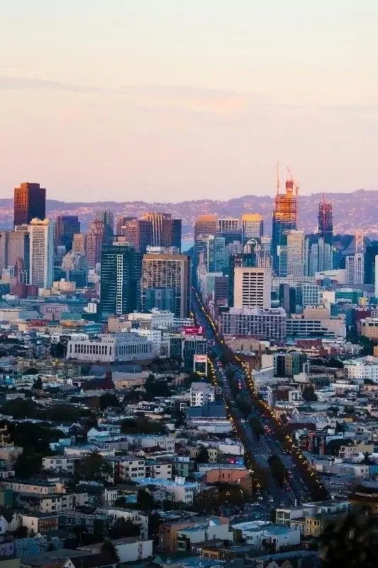 San Francisco's skyline at dusk seen from a hill, with freeway light trails running through residential streets in the foreground