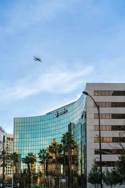 Zoom's headquarters building in San Jose, a curved glass office tower with the Zoom logo, palm trees reflected in the glass
