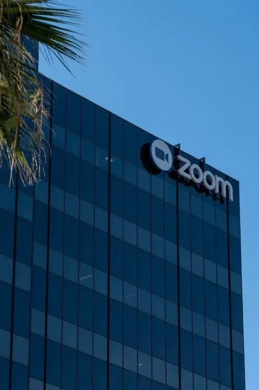 Close-up of the Zoom logo mounted on the corner of its glass headquarters tower in San Jose, palm fronds in the foreground