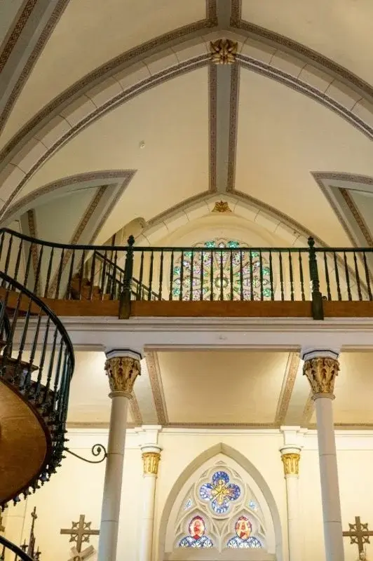The vaulted ceiling, stained-glass rose window, and edge of the spiral staircase inside Loretto Chapel in Santa Fe