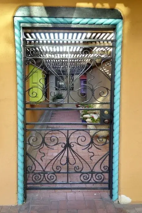 An ornate turquoise-trimmed iron gate in Santa Fe, wrought scrollwork framing a private courtyard beyond