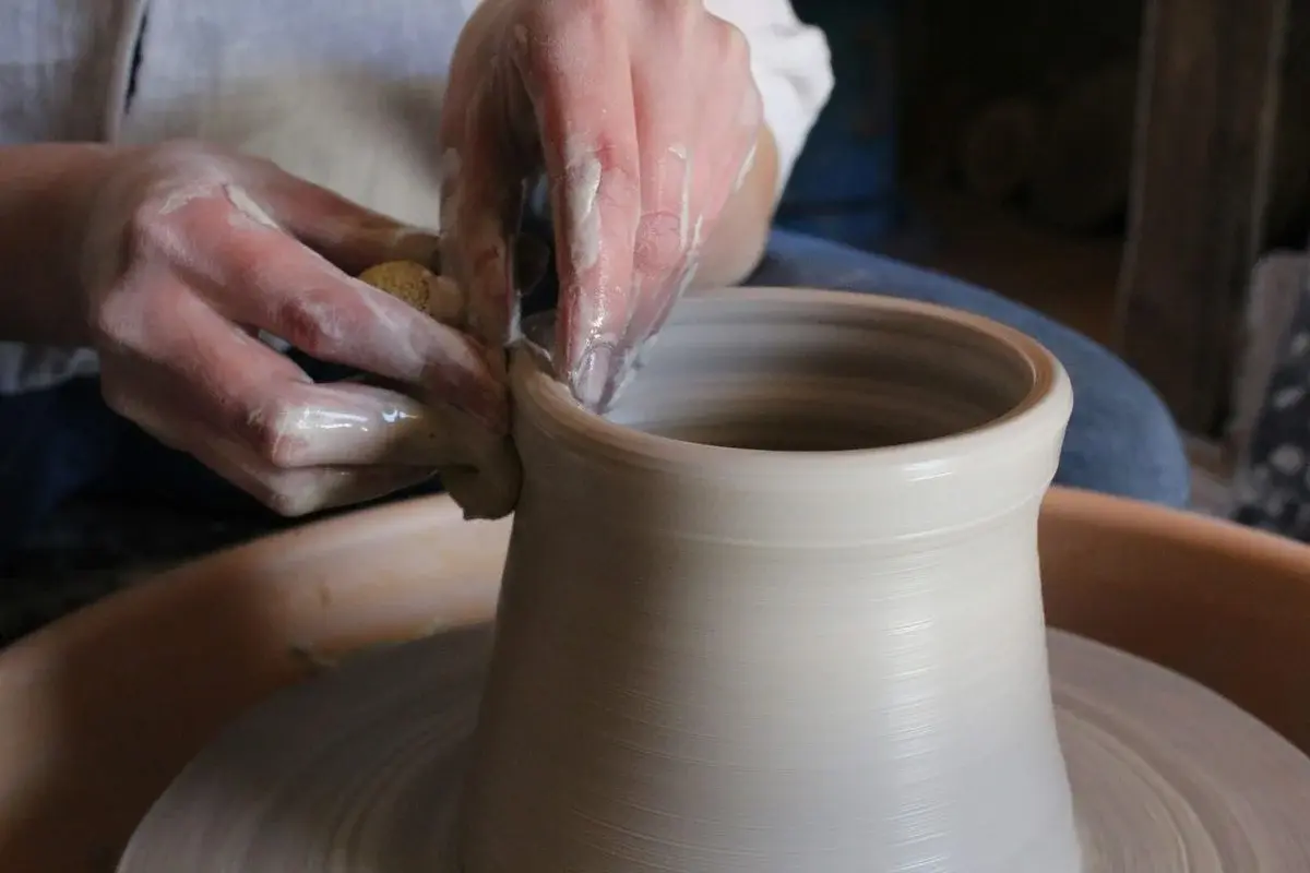 Two hands with a sponge shaping the rim of a pale clay vessel on a wheel in a Santa Fe studio